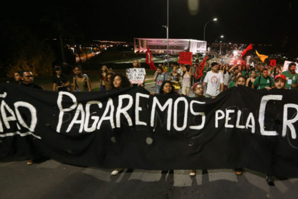 Foto de manifestação contra a PEC 55 em Brasília, na qual, um grupo de manifestantes segura uma faixa preta com a seguinte inscrição: "Não pagaremos pela crise!".