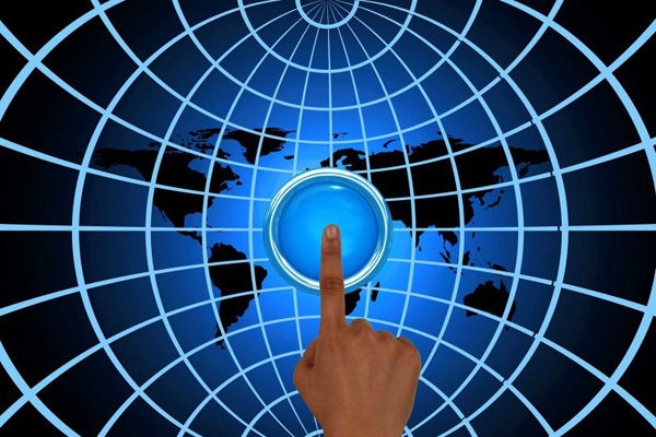 Imagem de uma mão clicando em um botão sobre o mapa do mundo, representando a interligação do globo por meio da internet