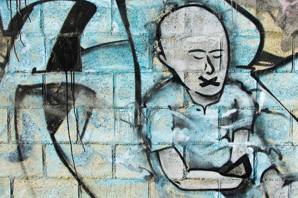 Pintura artística em muro de rua de menino com mordaça