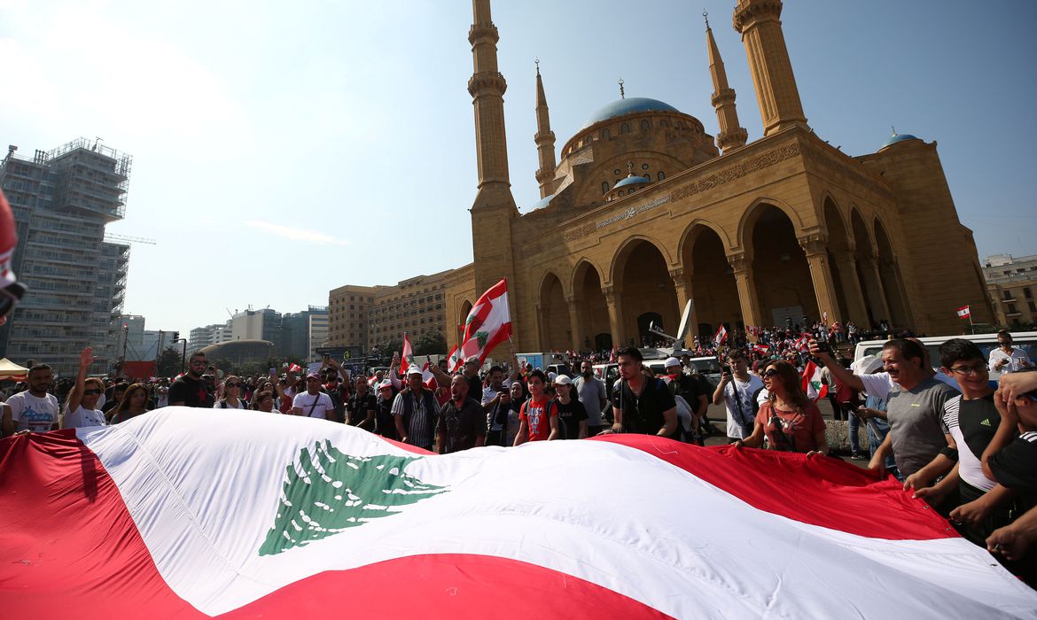 Em uma praça de Beirute, pessoas se reúnem e seguram uma ampla bandeira do Líbano