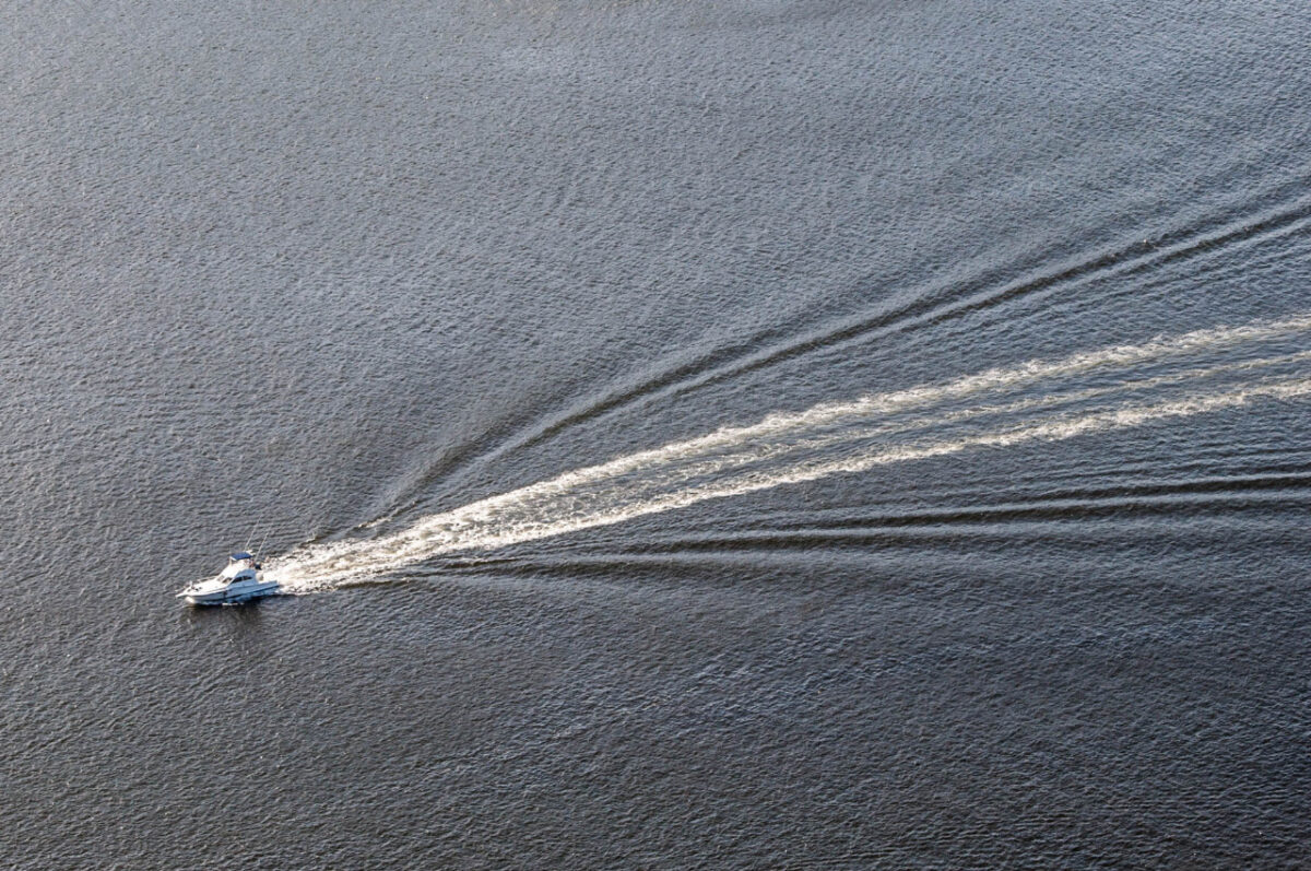 Visão aérea do oceano com um barco se deslocando para a esquerda e deixando rastro do movimento