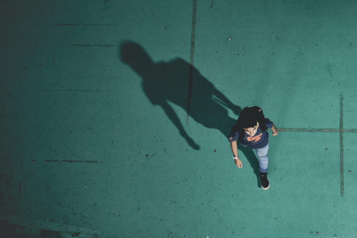 Visto de cima, estudante caminha, enquanto sua sombra é projetada