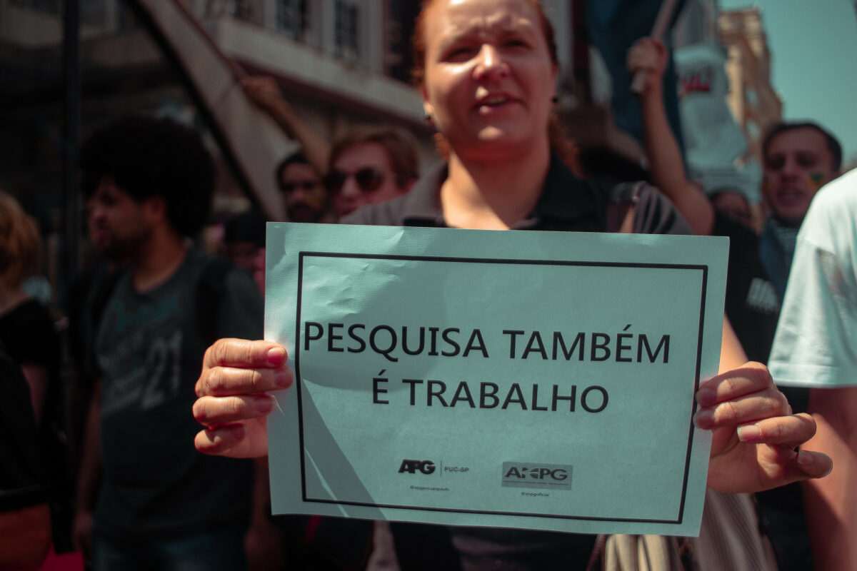 Em uma manifestação de rua realizada em 2019, estudante mostra um cartaz com os dizeres "pesquisa é trabalho"