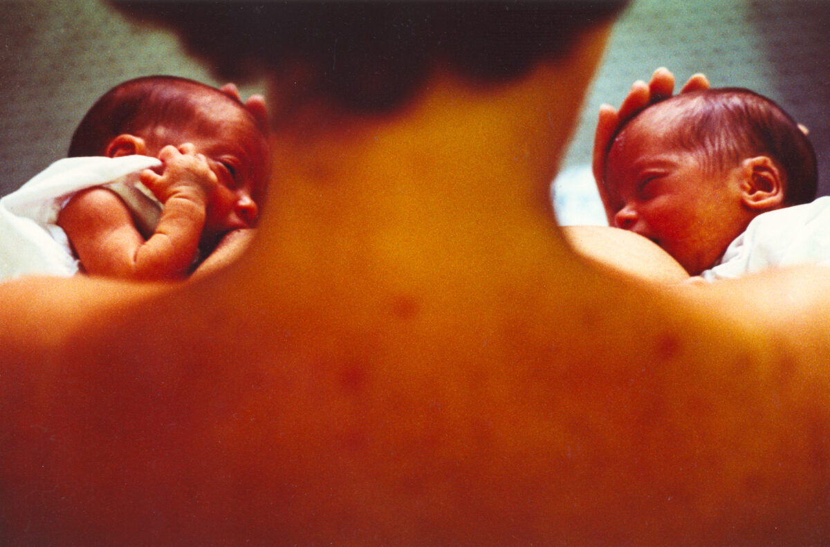 Mulher de costas amamenta bebês gêmeos, um em cada seio