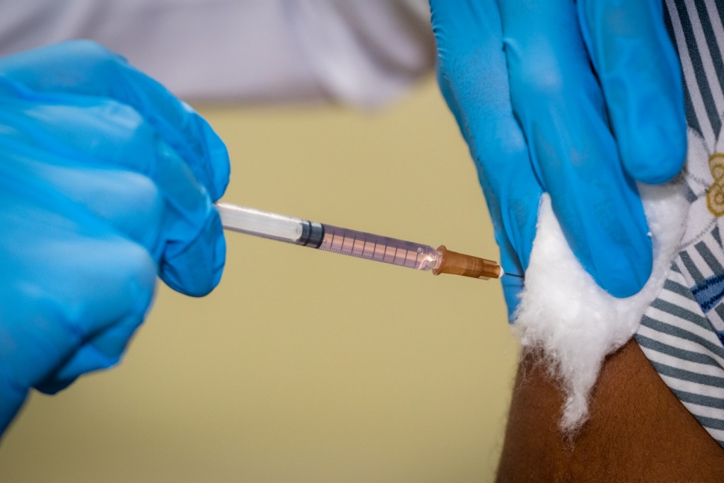 Mãos de um profissional da saúde com luvas azuis aplica vacina em paciente