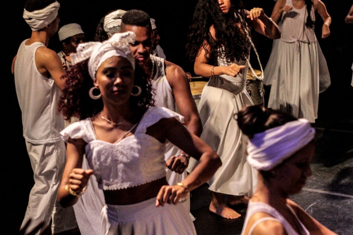 Performance do grupo Pade. Várias pessoas vestidas de branco em uma apresentação de dança africana.