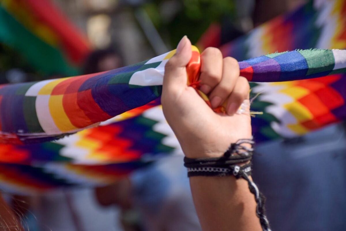 Plano fechado em uma mão que segura as pontas de uma bandeira quadriculada e com as cores do arco-íris