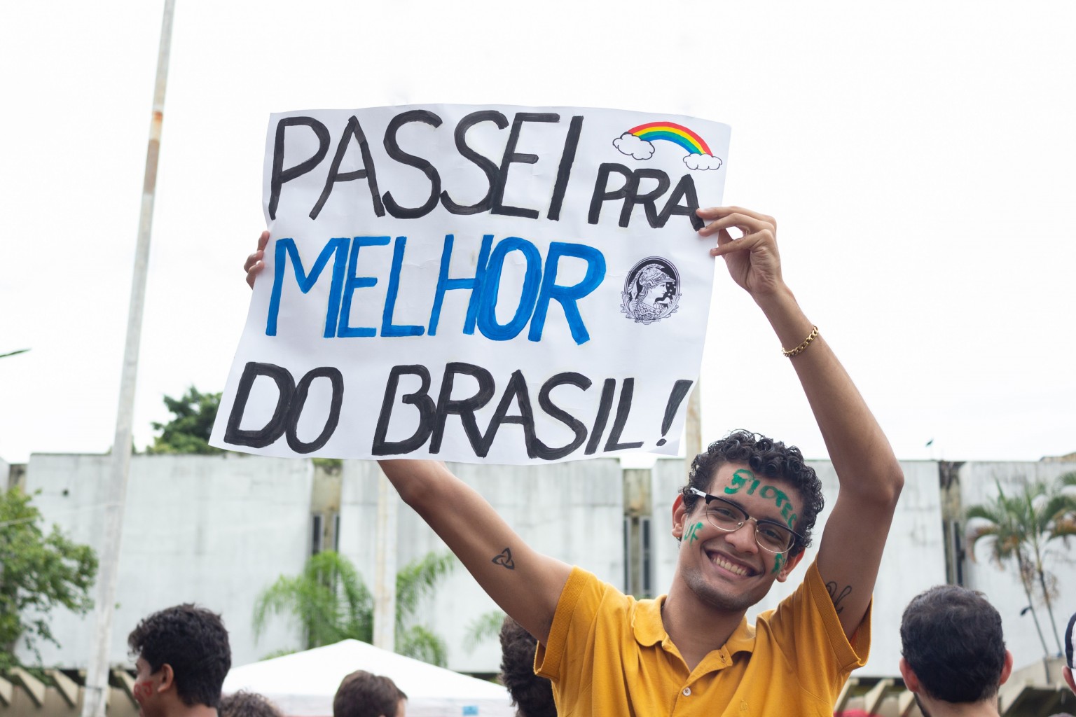 Estudante comemora aprovação para faculdade na UFRJ e segura cartolina em que está escrito "Passei para a melhor do Brasil!"