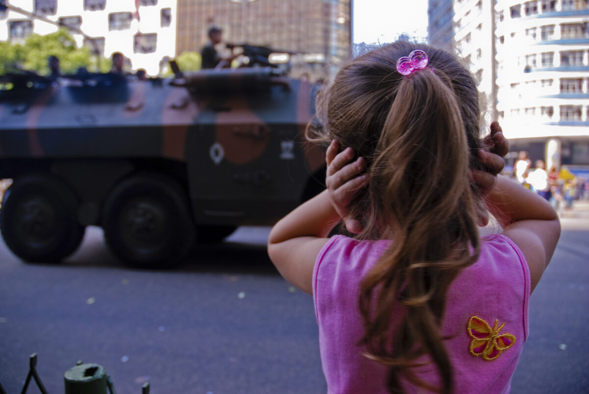 Na Avenida Presidente Vargas, durante um desfile militar, criança protege os ouvidos e a cabeça diante de um veículo de guerra