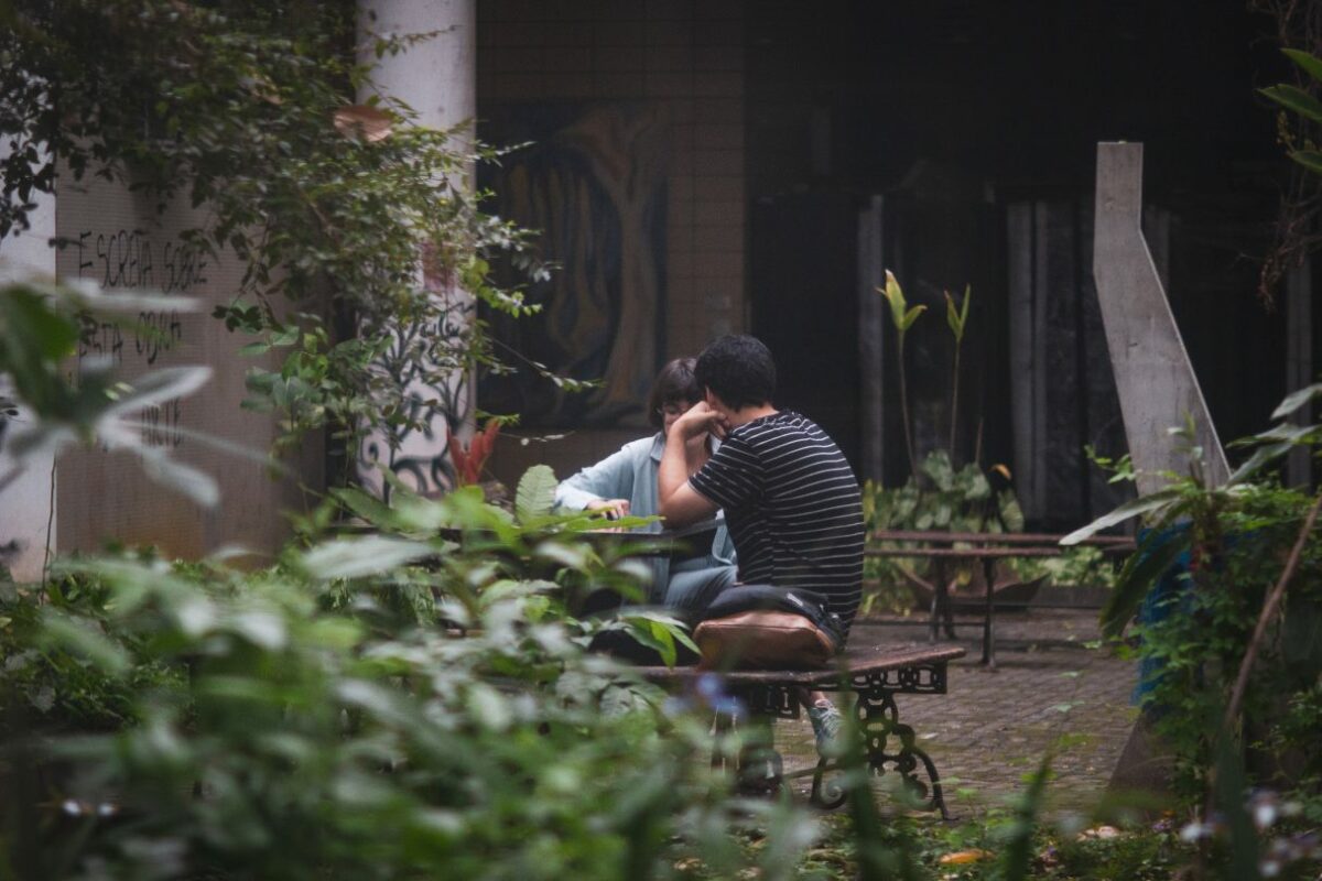 Dois estudantes conversam sentados em bancos no jardim da Reitoria
