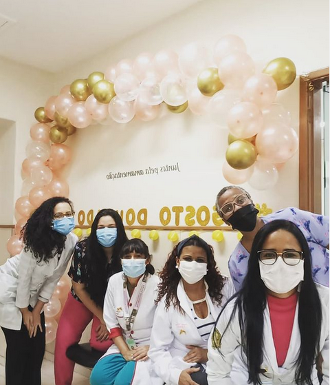 Seis profissionais de saúde com máscaras posam para foto em frente à decoração de Agosto Dourado na maternidade