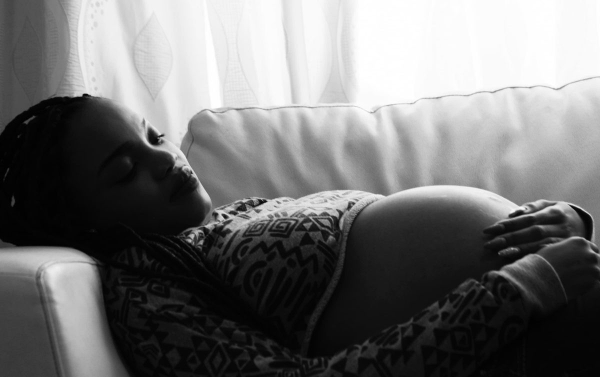 Foto em preto e branco de uma gestante deitada em um sofá. Ela acaricia a barriga.