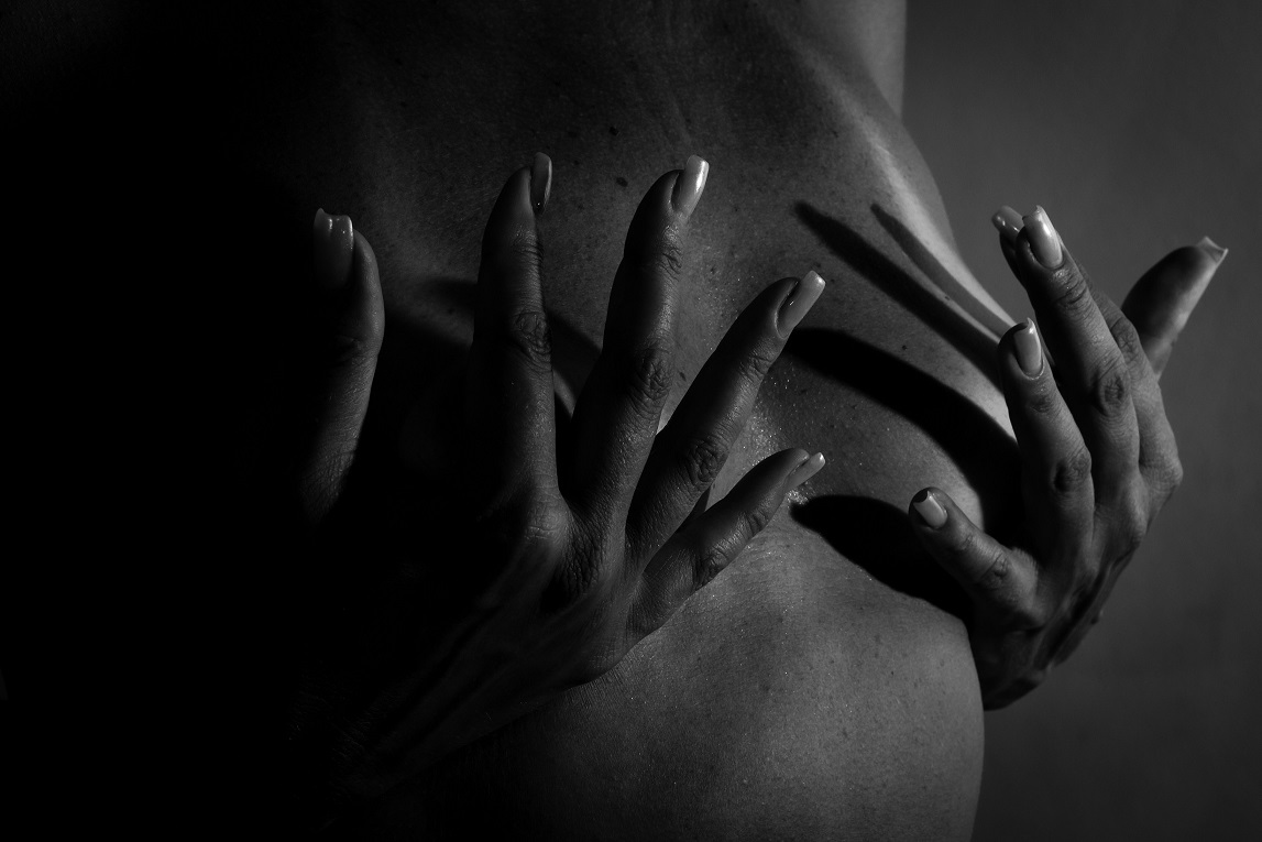 Foto em preto e branco. Mulher cobre as mamas com as mãos.
