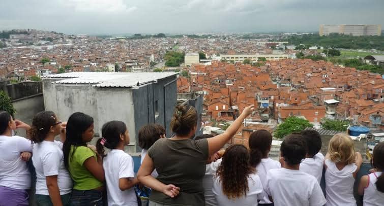 Do alto de uma laje, um grupo de estudantes e professora avista a favela