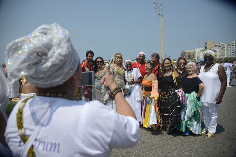 Uma mulher veste roupas brancas e, de costas para a cãmera, faz a foto de um grupo de pessoas de diferentes religiões