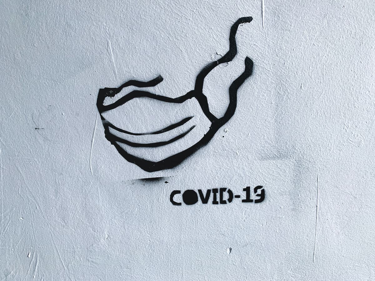 Em fundo branco, um graffite de uma máscara e a palavra covid-19
