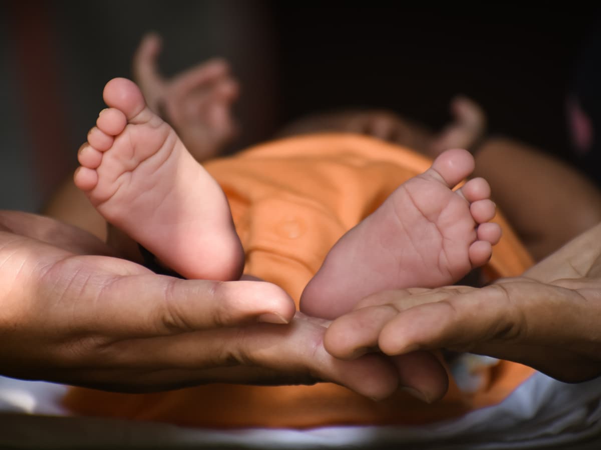 Foto mostra mãos de um adulto segurando os pés de um bebê