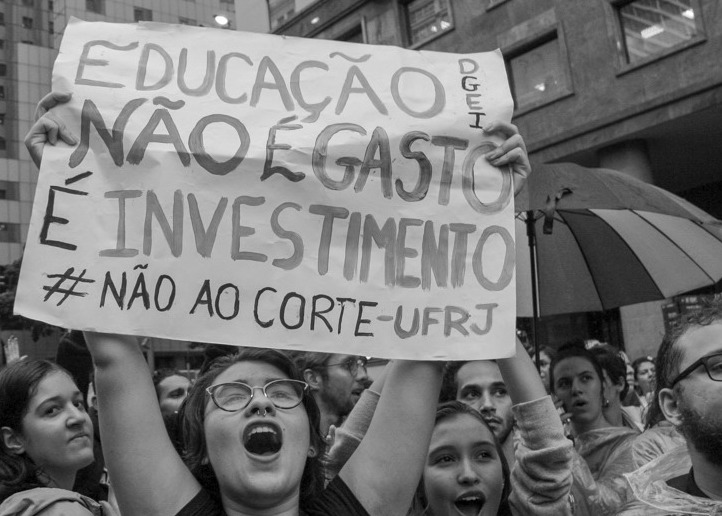 Em meio a um protesto, estudante segura um cartaz onde se lê "educação não é gasto, é investimento - não ao corte UFRJ"