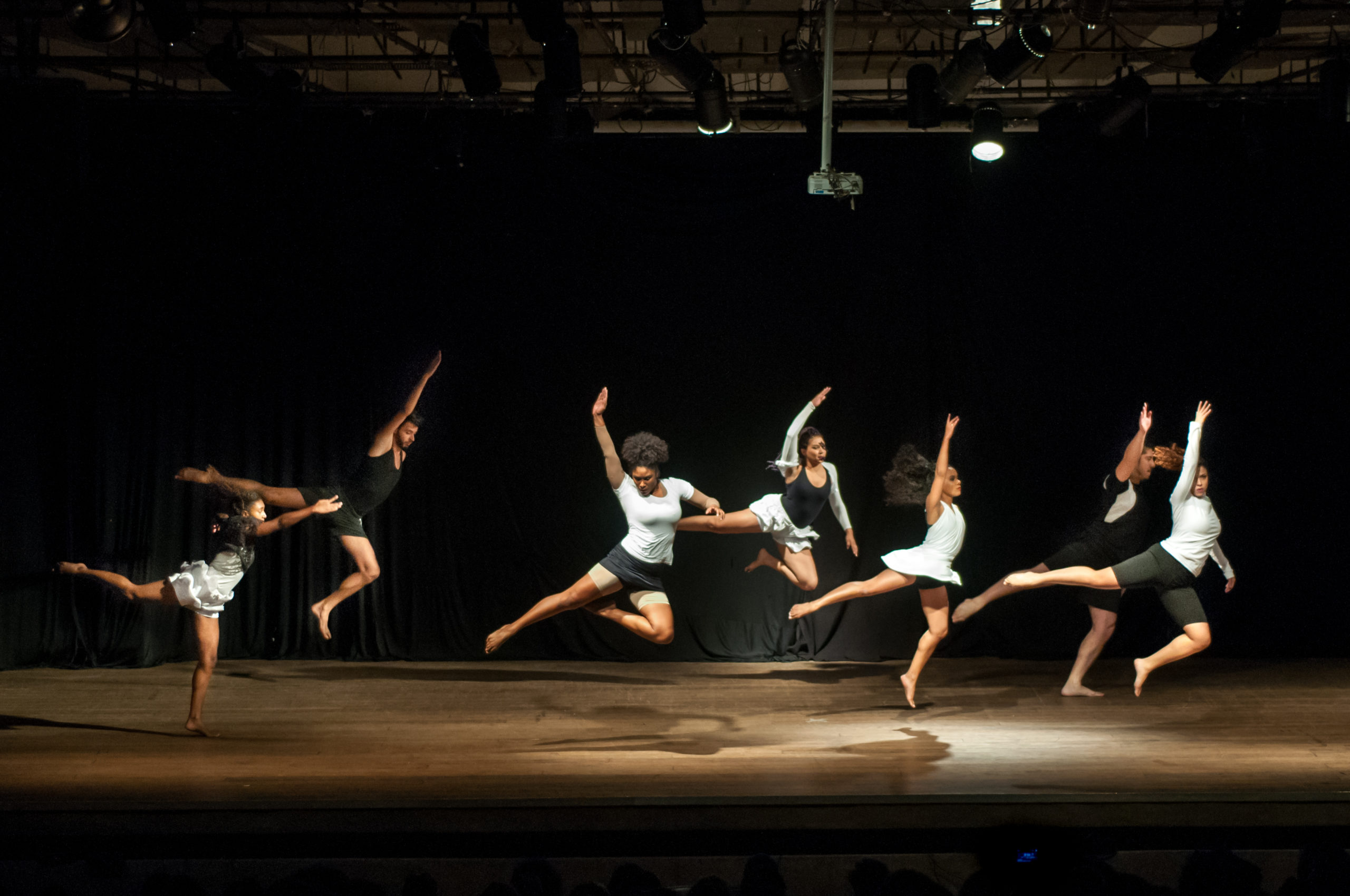 Grupo de dança com seis mulheres faz movimentos sincronizados de salto no palco
