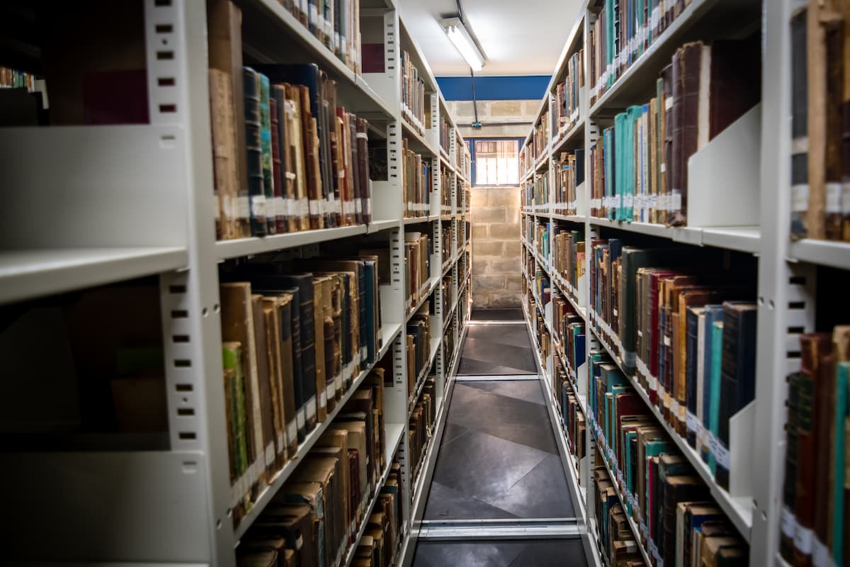 Fotografia de um corredor da biblioteca formado por fileiras de estantes cheias de livros antigos.
