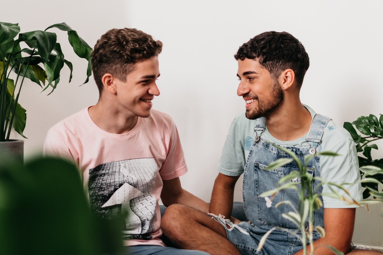 Um casal de dois homens sorriem, entre plantas