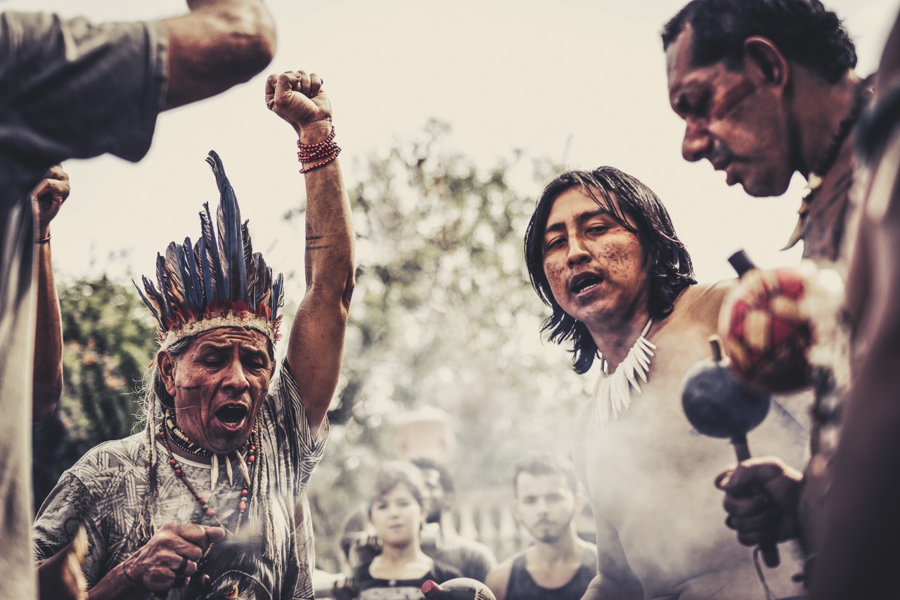 um grupo de pessoas indígenas estão em um círculo realizando manifestação cultural