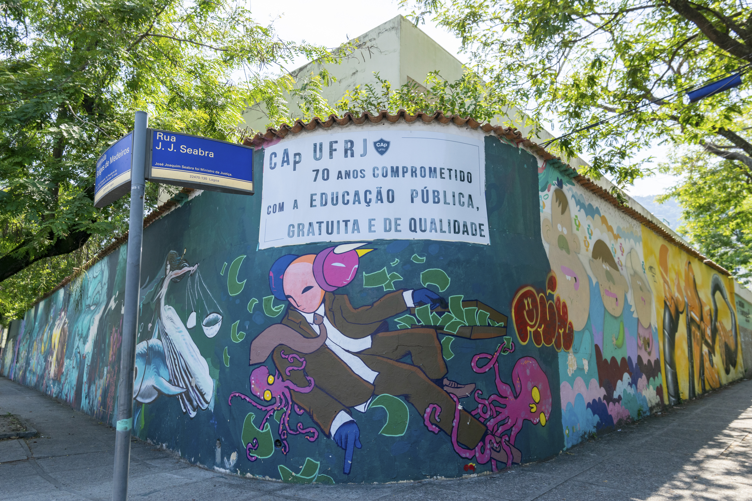 Em uma parede grafittada, pode-se ler a frase "CAp UFRJ, 70 anos comprometido com a educação pública, gratuita e de qualidade.