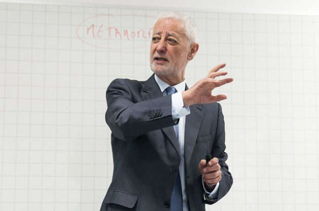 António Nóvoa, um senhor branco com cabelos e barba branca, veste terno e gravata e fala em frente a um quadro branco.