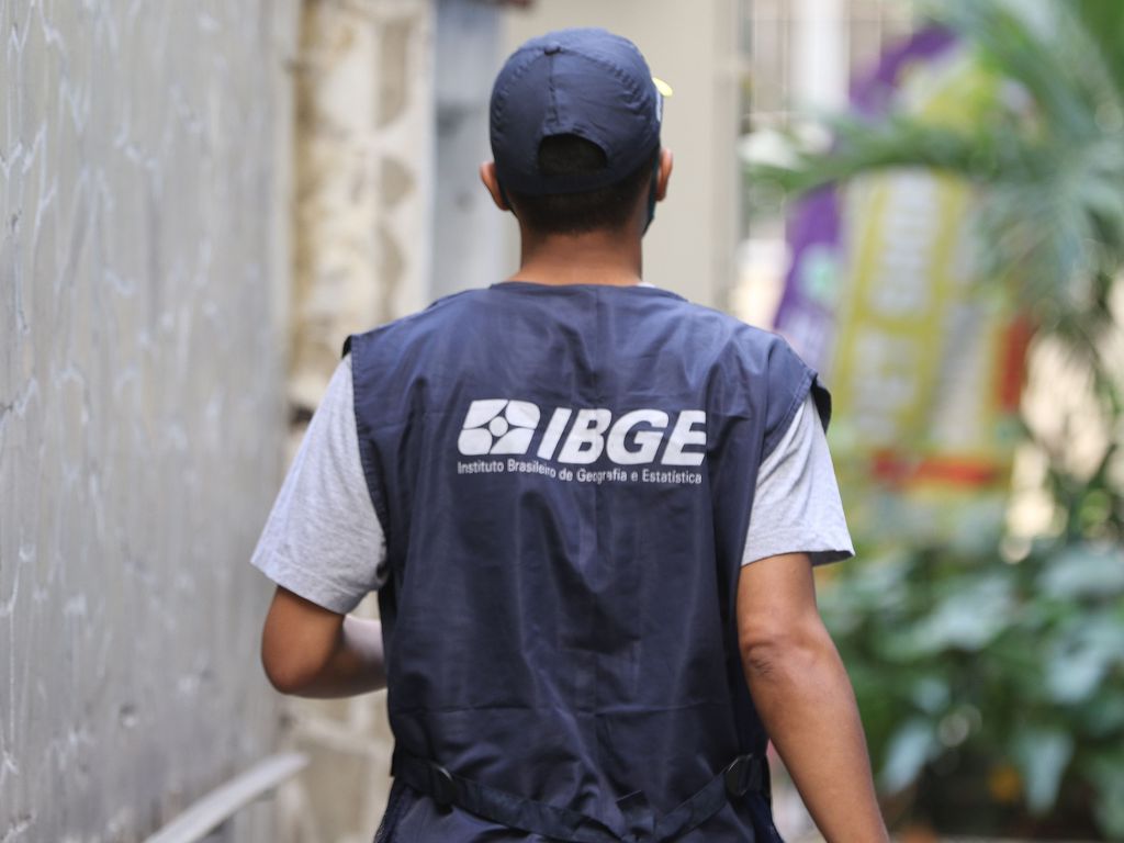 Recenseador de costas veste colete. Nas costas, pode-se ver a logo do IBGE.