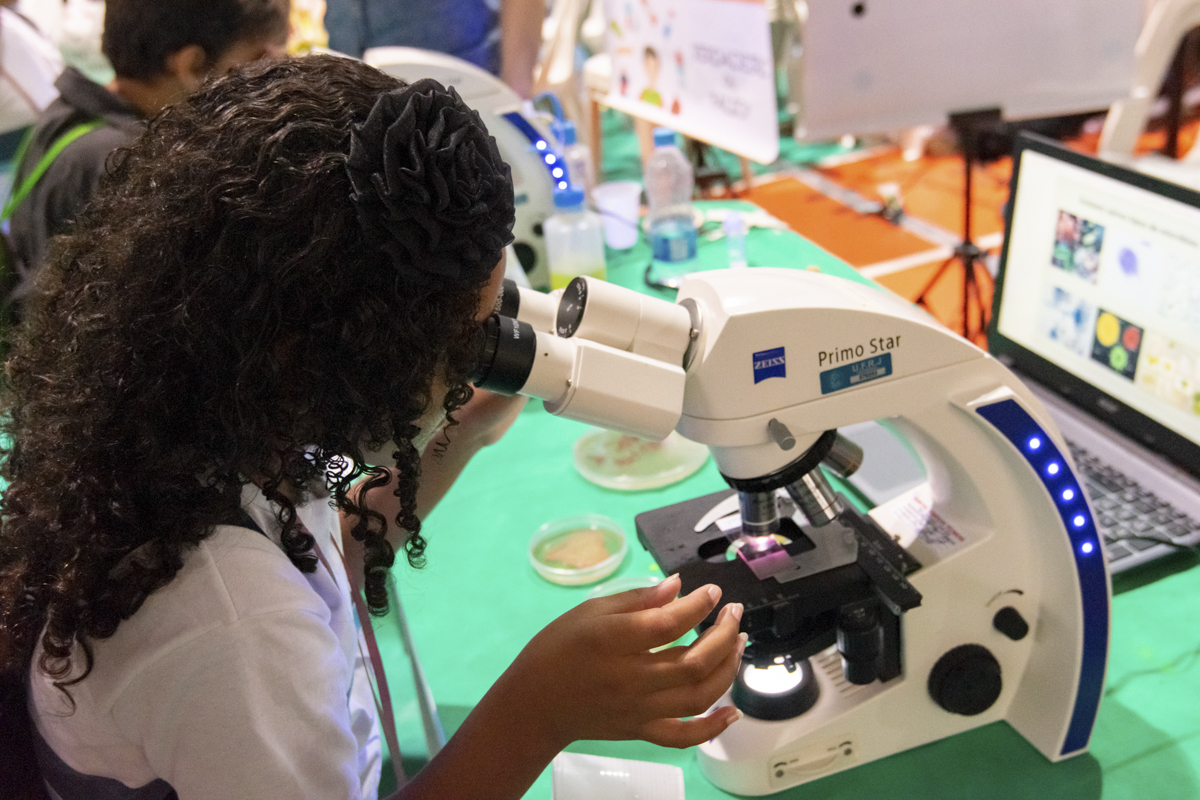 Menina observa um experimento através da lente de um microscópio.