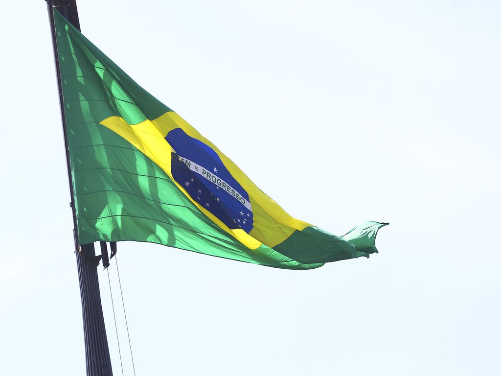 A bandeira do Brasil tremula em frente a um céu azul claro.