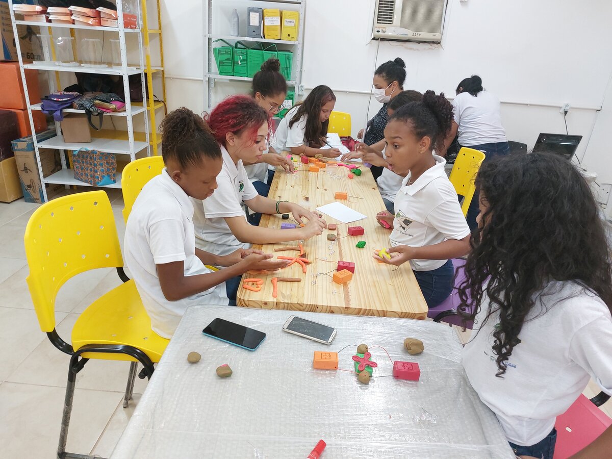 Na foto, grupo de alunas sentado à mesa interage com uma das oficinas do projeto de extensão.