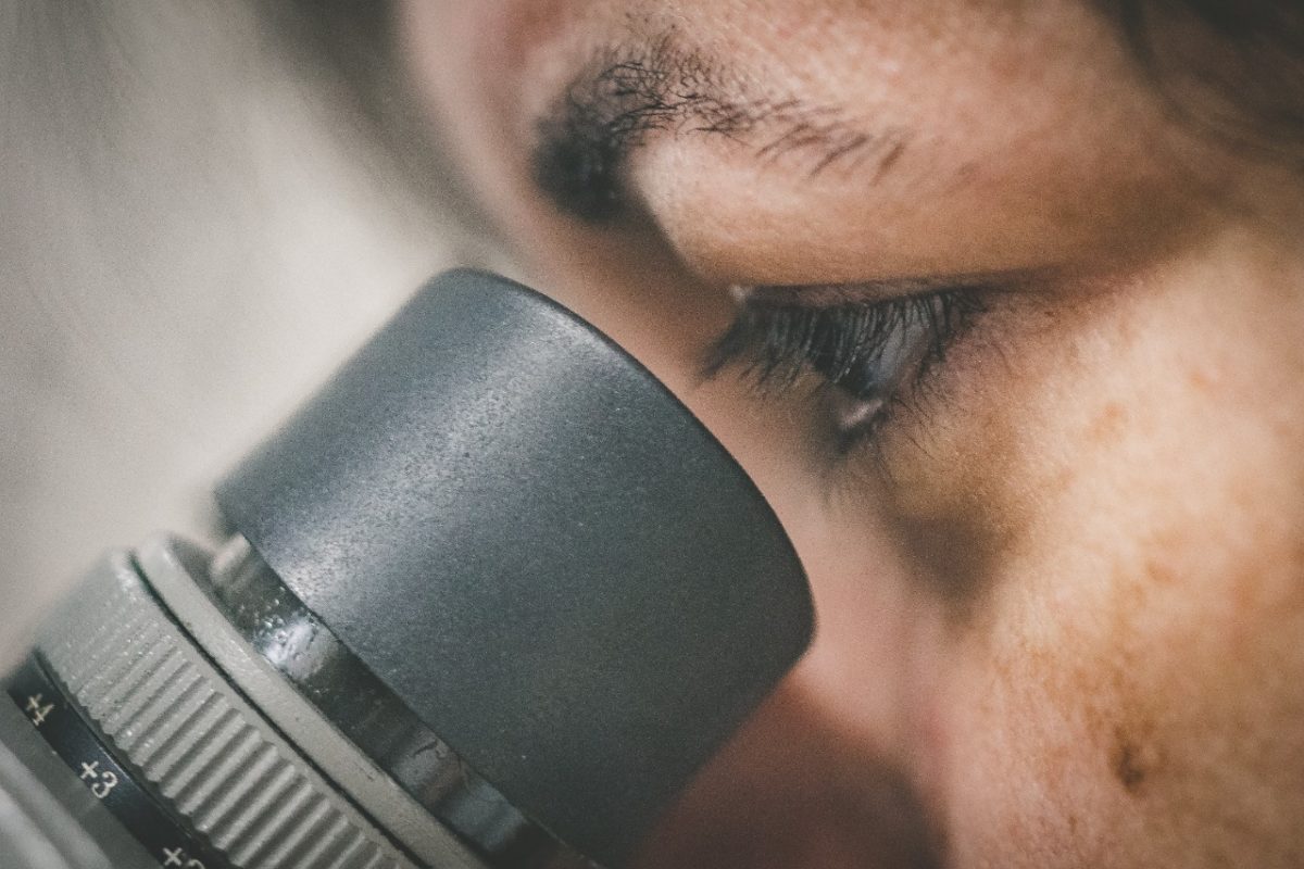 Foto em close do olho de uma pessoa observando algo através da lente de um microscópio.