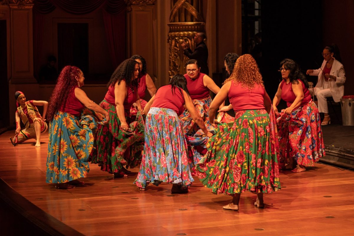 Mulheres dançam no palco do Theatro Municipal. Elas usam blusa vermelha e saia colorida.