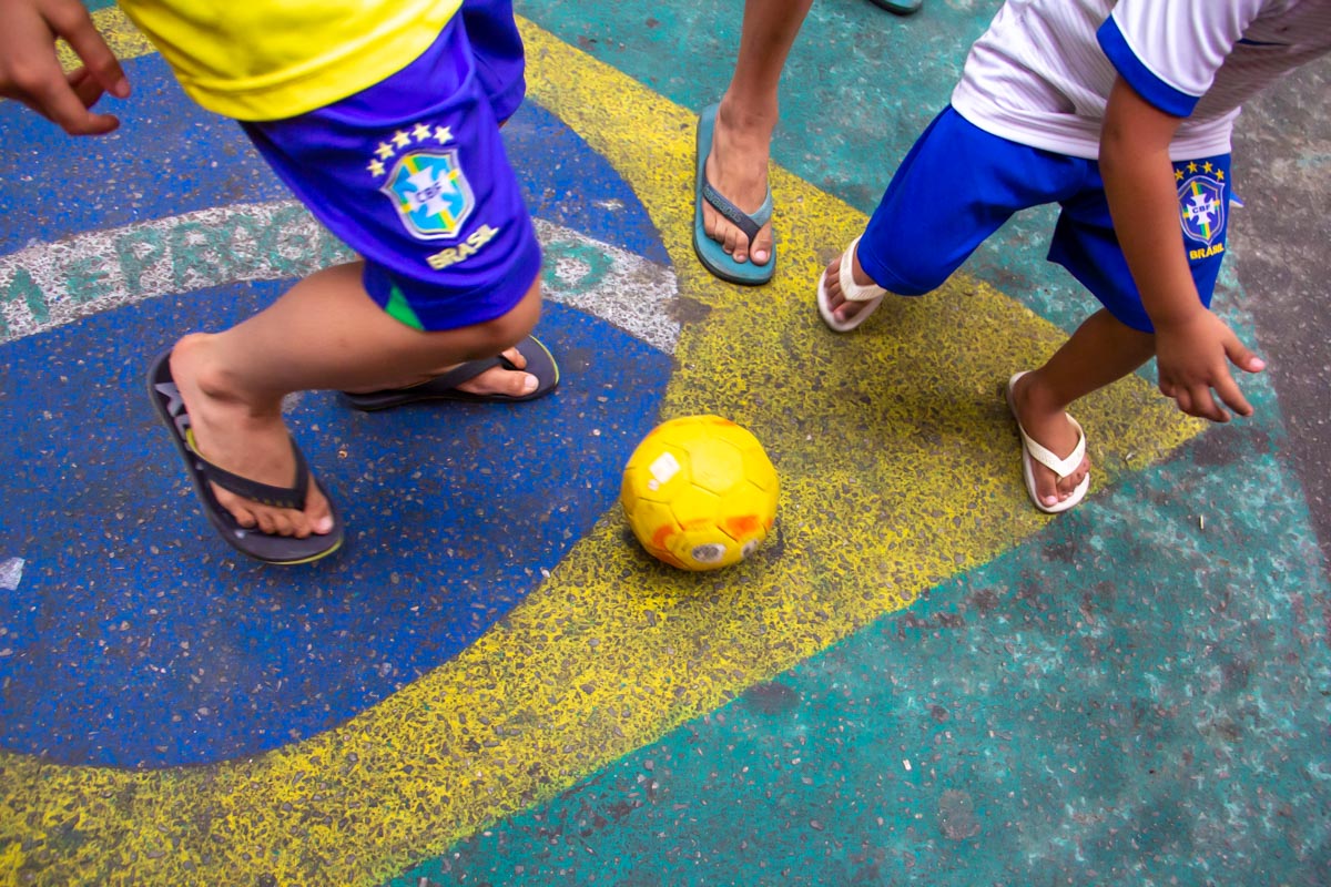 pés de crianças jogando bola sobre uma pintura da bandeira do Brasil no chão