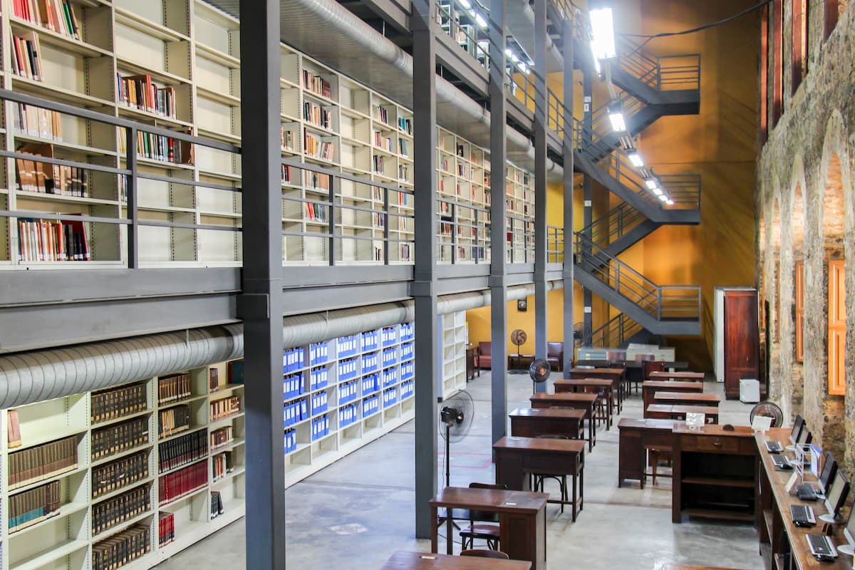 Fotografia da biblioteca do Instituto de Filosofia e Ciências Sociais. À esquerda, há um mezanino de dois andares com estantes repletas de livros. À direita da imagem, mesas estão distribuídas por todo o salão.