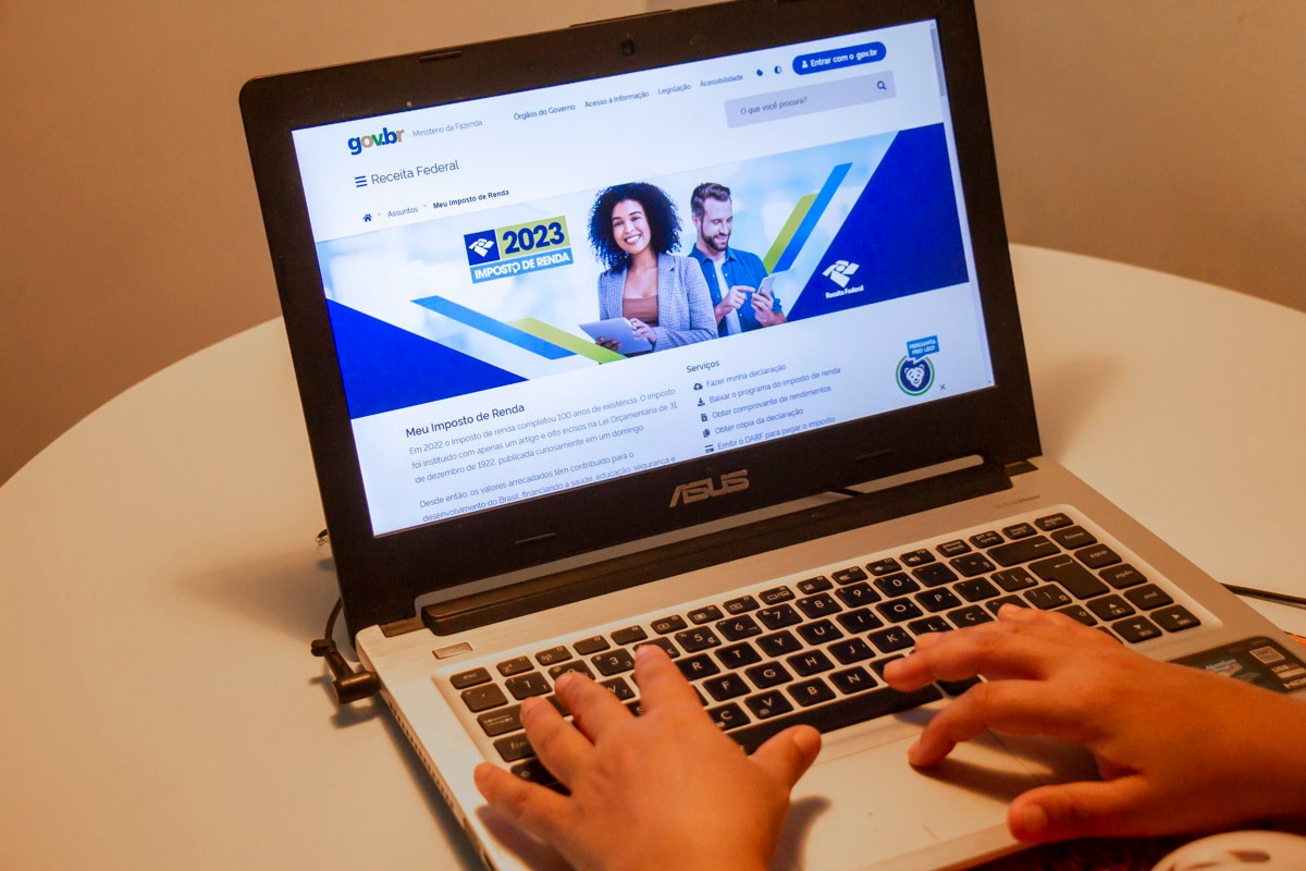 Foto mostra um laptop com tela aberta na página da Receita Federal. Duas mãos utilizam o aparelho.