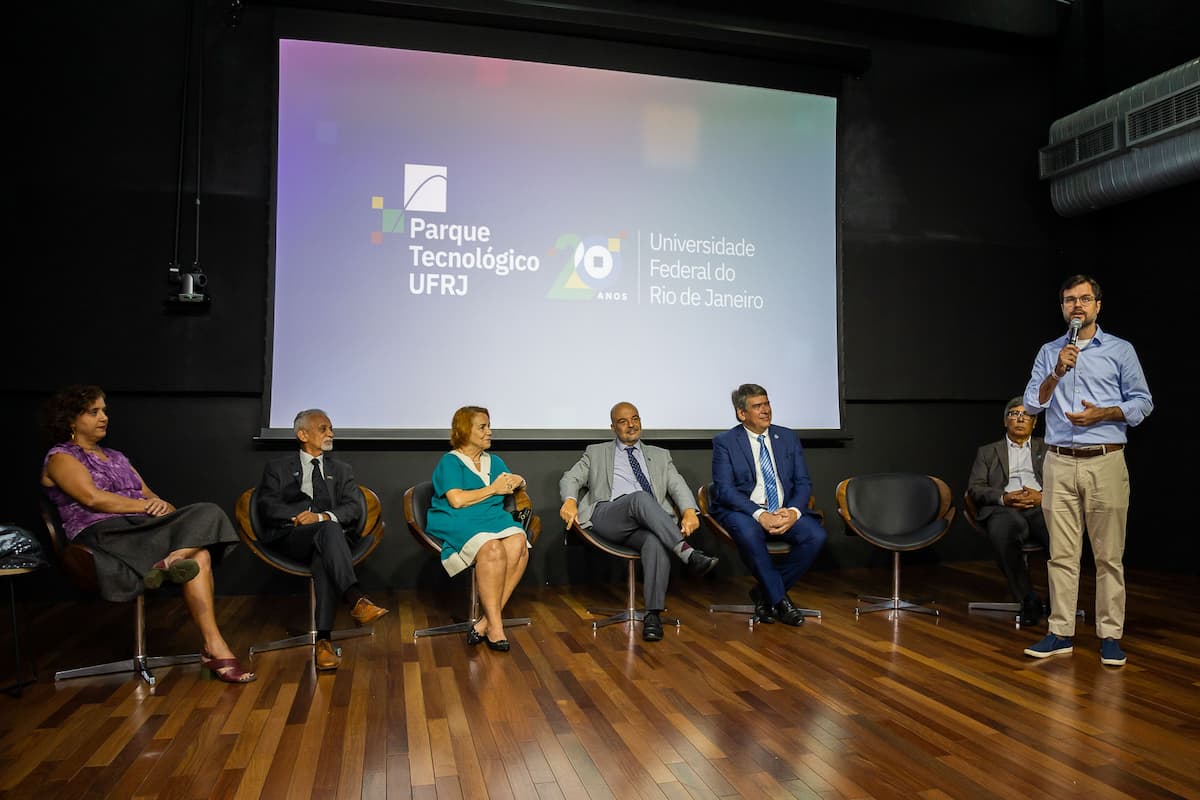 Fotografia da solenidade realizada no auditório da Inovateca, No palco estão Tatiana Roque, José Antônio Silvério, Marina Esteves, Carlos Frederico da Rocha Leão, Vicente Ferreira, Elias Ramos e Chicão Bulhões. Atrás deles, no telão, está o logotipo comemorativo de 20 anos do Parque Tecnológico.