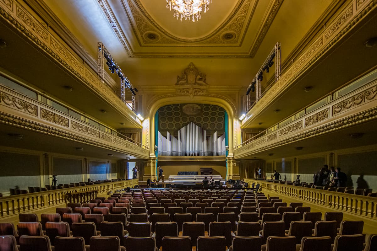 Fotografia do Salão Leopoldo Miguez, na Escola de Música da UFRJ. Em primeiro plano, fileiras de cadeira da plateia. Ao fundo, o palco com destaque para o órgão Tamburini.