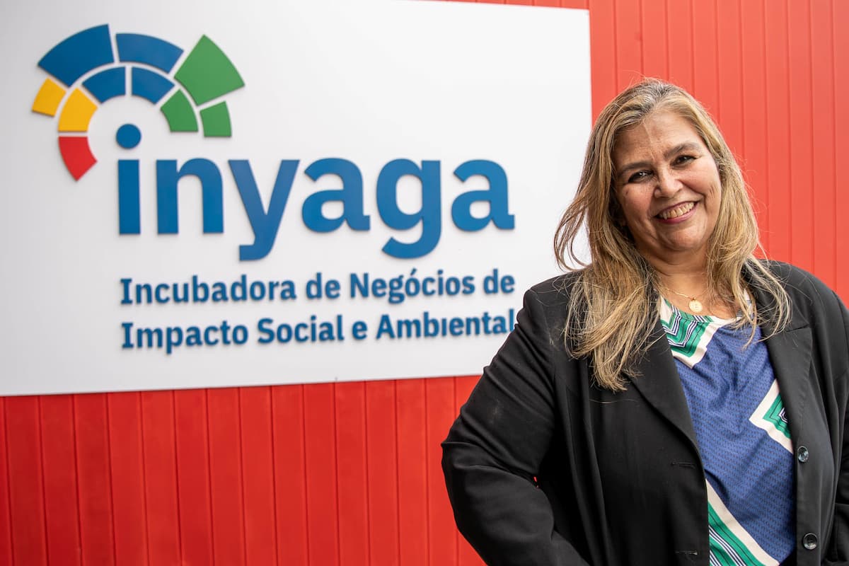 Fotografia mostra a professora Eliane Ribeiro em frente ao letreiro onde se l:e Inyaga incubadora de negócios de impacto social e ambiental.