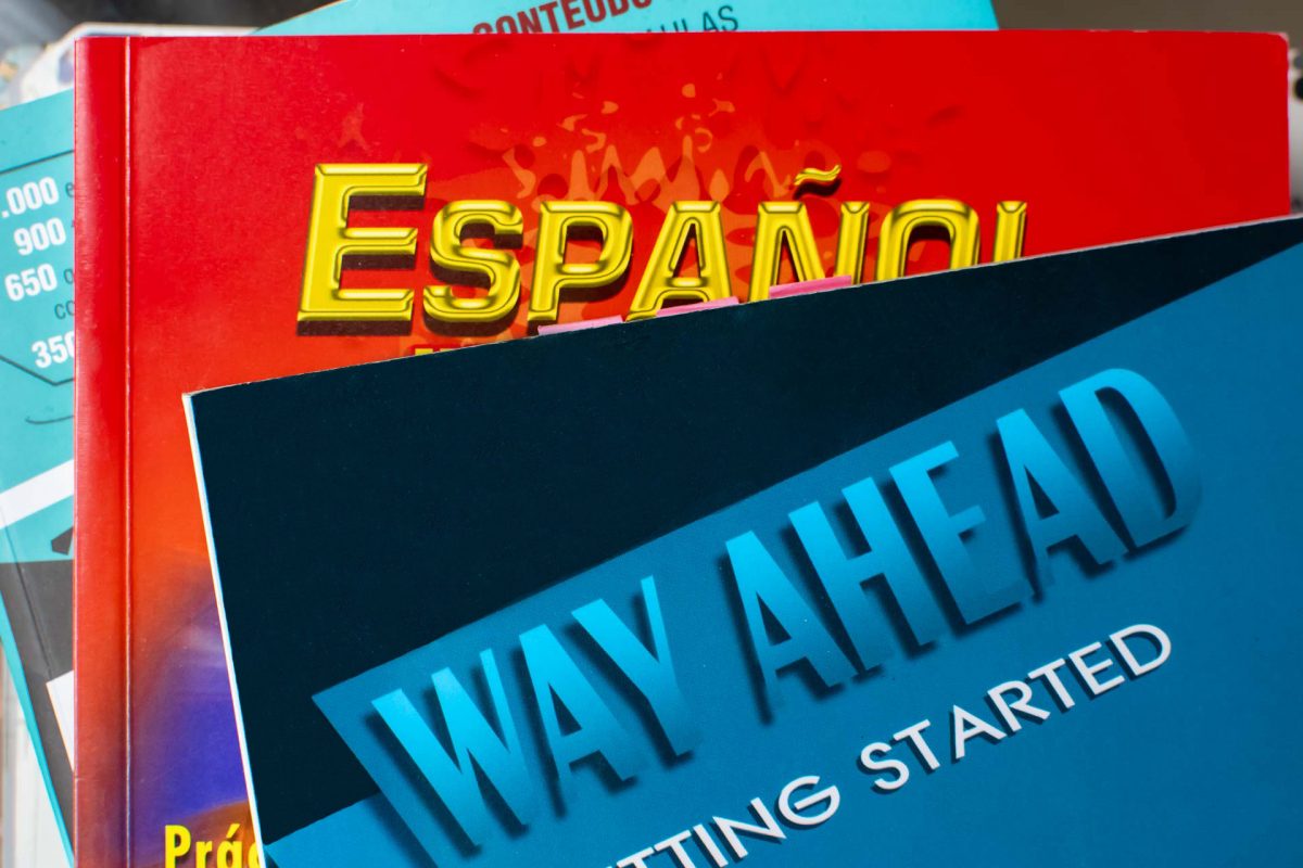 Fotografia mostra livros de diferentes línguas empilhados. Na frente, um exemplar na cor azul traz o título “Way Ahead - Getting Started”. Abaixo dele, está um exemplar vermelho com o título “Español” em amarelo.