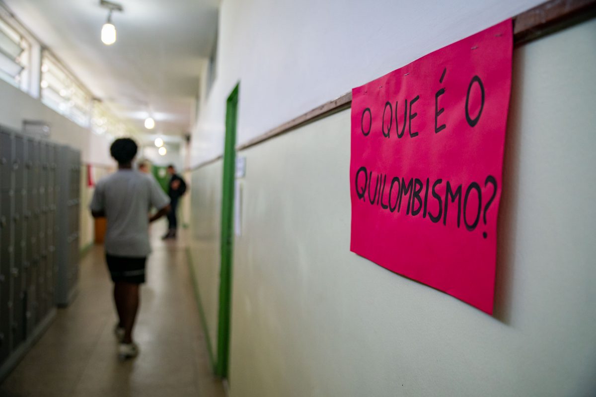 Corredor com um jovem negro caminhando e um cartaz escrito "O que é quilombismo?"