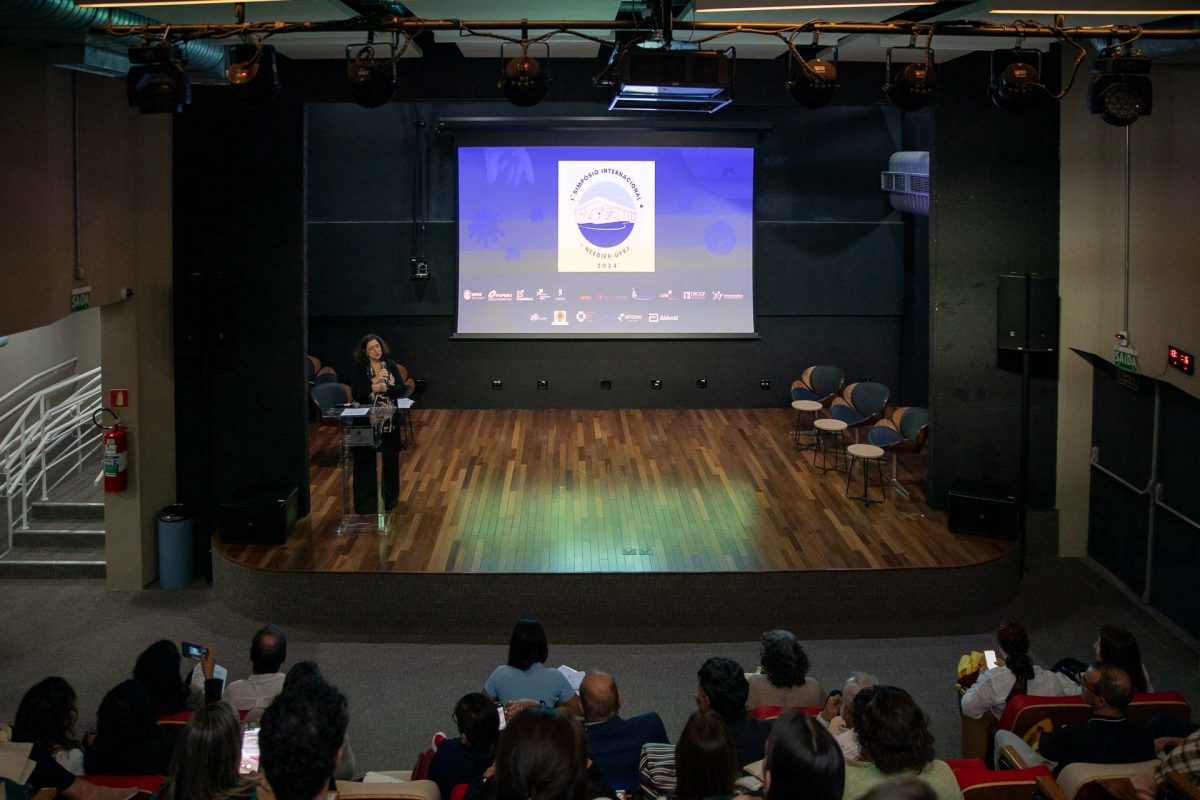 Fotografia de um auditório. No telão, lê-se "Primeiro Simpósio Internacional Needier UFRJ".