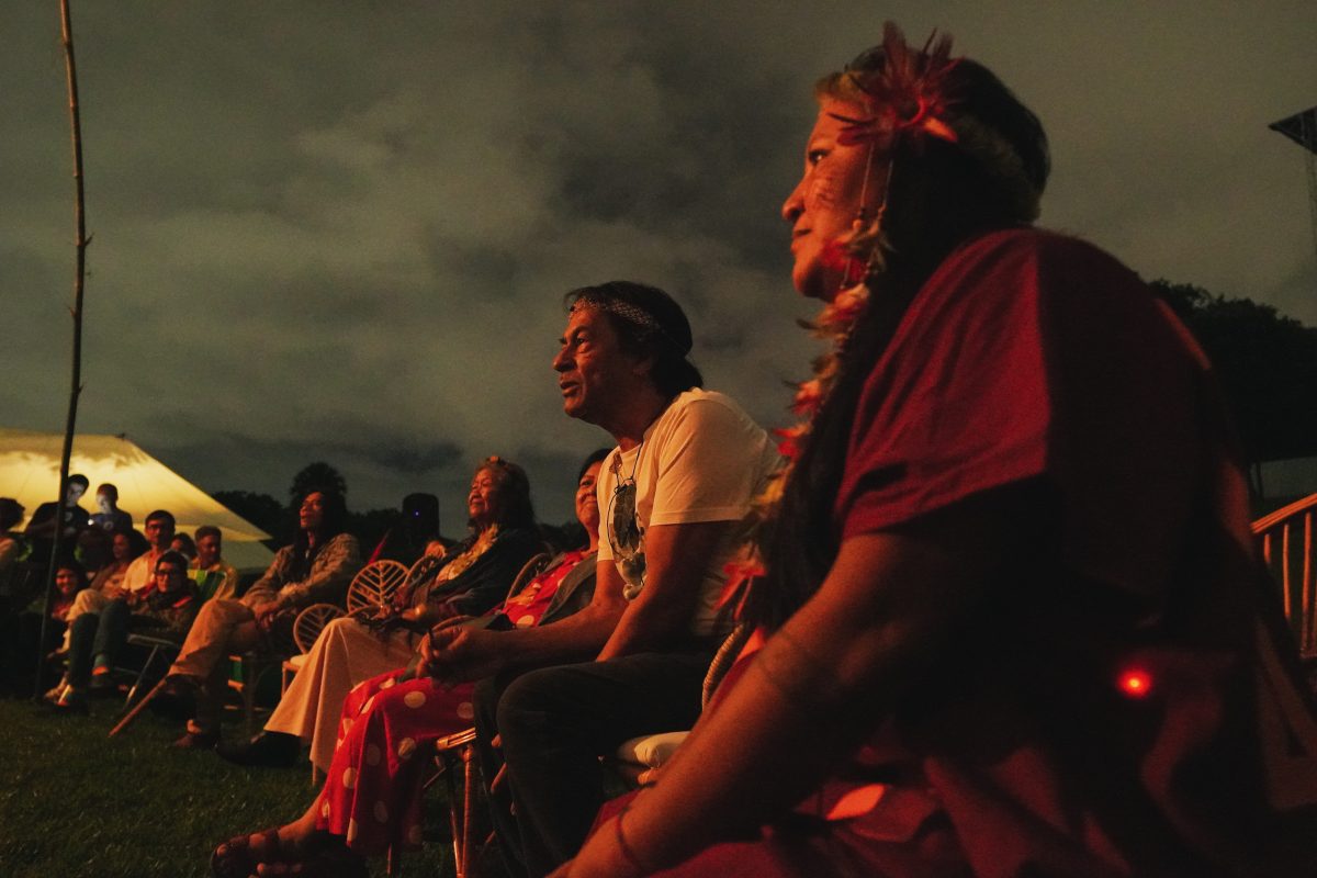 Grupo de pessoas indígenas reunidas em roda a céu aberto durante a noite