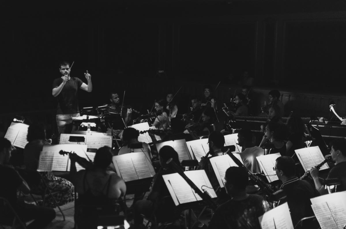 A imagem, em preto e branco, apresenta uma orquestra tocando.