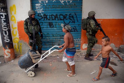 Foto colorida de Fuzileiros Navais que participam de operação numa favela da zona norte do Rio de Janeiro, observados por crianças.