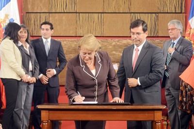 Foto colorida de Miclelle Bachelet, presidenta do Chile, assinando a lei do ensino superior gratuito e universal.